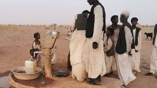 In einer wüstenartigen Landschaft umstehen Männer einen Zapfhahn für Wasser.