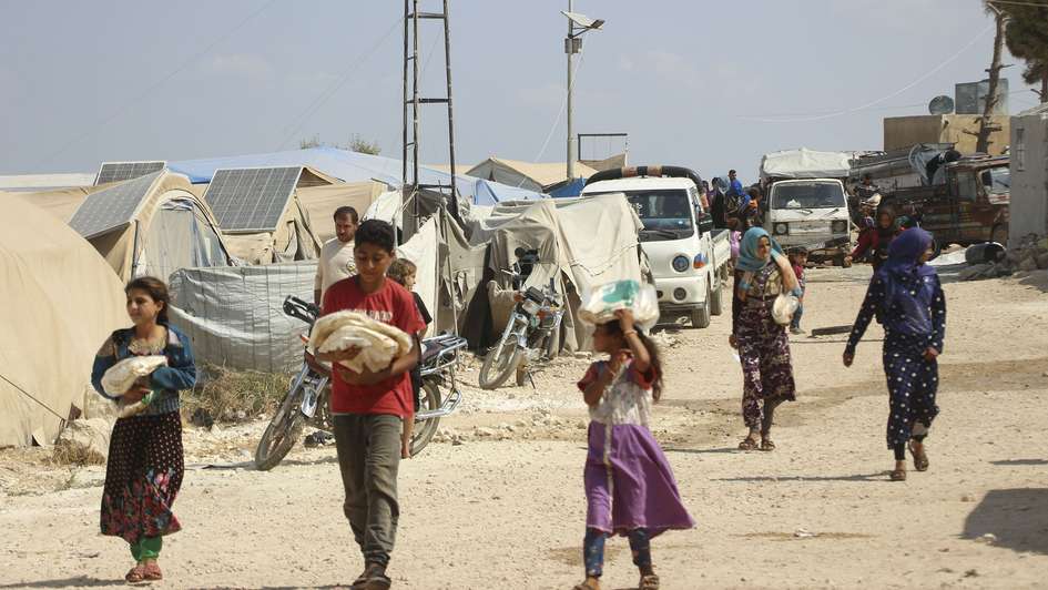 Refugees carry bags of bread in a refugee camp