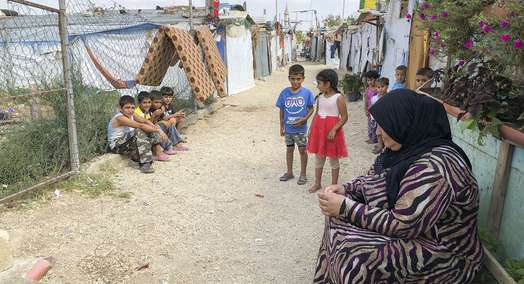 Eine Frau und mehrere Kinder sitzen und stehen auf einem Weg durch ein Camp für syrische Flüchtlinge im Libanon.